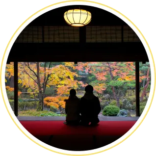 和室の畳の上から、開け放たれた障子越しに美しく紅葉した日本庭園を眺める二人の後ろ姿。