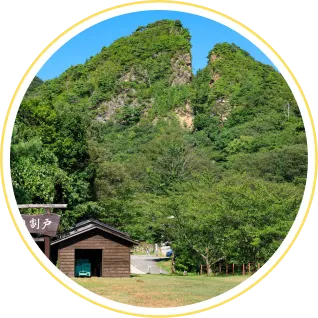 青々とした木々が生い茂る中に、中央が大きくV字に割れた特徴的な岩山（佐渡の金北山や景勝地）がそびえ立つ、自然豊かな佐渡の風景。