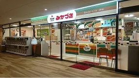 商業施設内にあるみかづき万代店の店舗外観。緑色の看板が掲げられ、ガラス張りの店内にはテーブルや椅子が並んでいる様子。